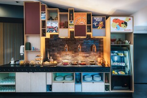 Una colazione a buffet con diversi cibi, una macchina del caffè e un frigorifero con bevande.