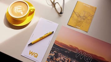 Una taza de café con arte de latte, un par de gafas, una libreta amarilla y un mapa impreso sobre una mesa.