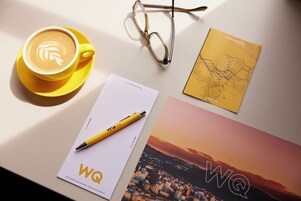 Una tazza di caffè con decorazioni in schiuma, un paio di occhiali, un quaderno giallo e una mappa stampata su un tavolo.