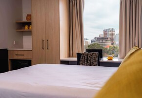 Una camera d'albergo con un letto, una scrivania e una finestra con tende.