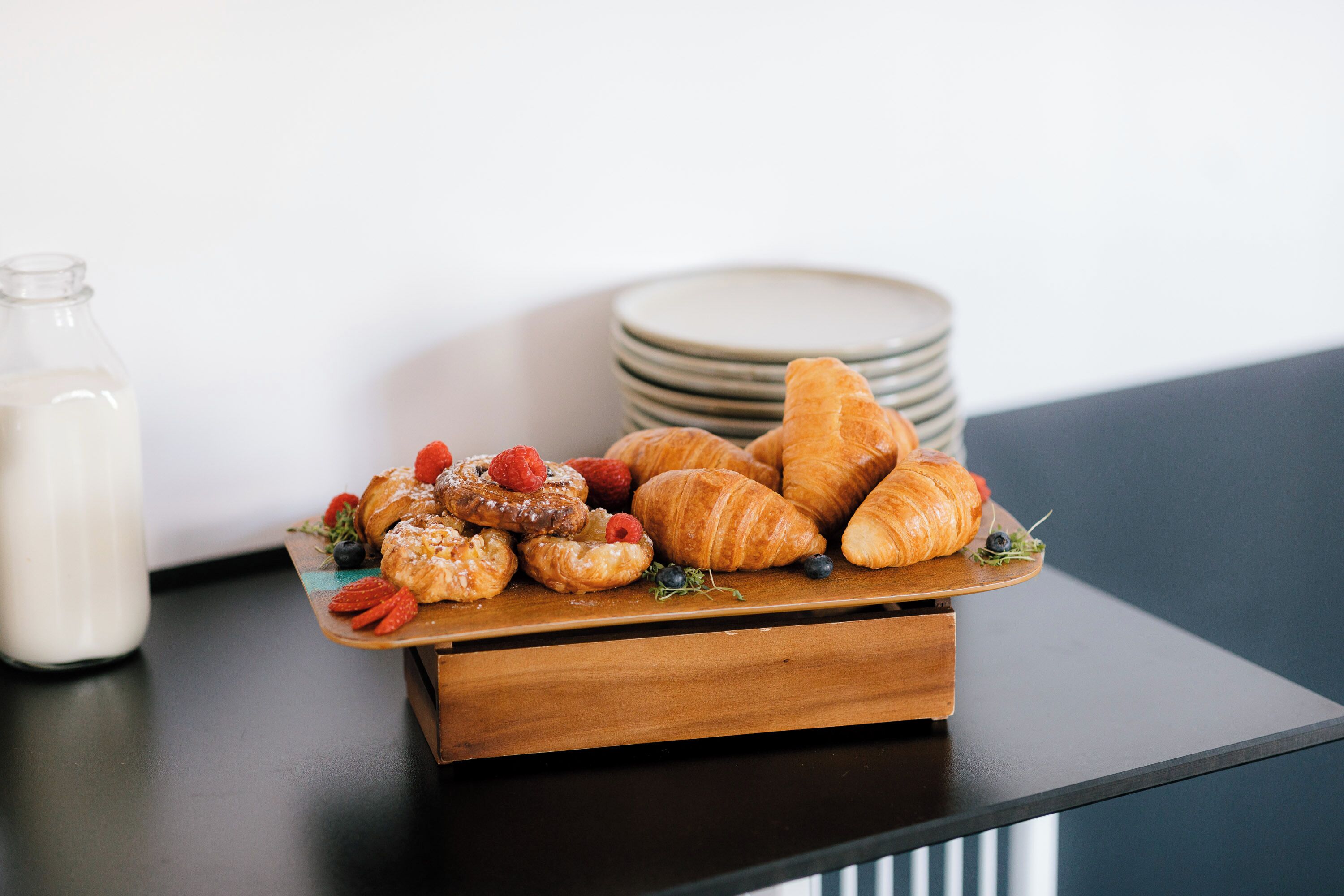 A wooden serving tray with pastries and berries on a table.