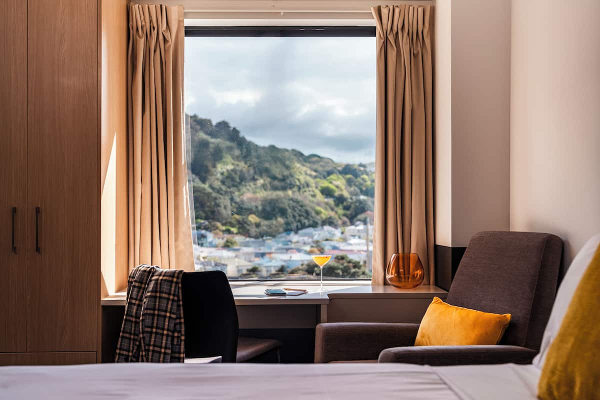 A hotel room with a bed, a desk, a chair, and a view of a hillside.