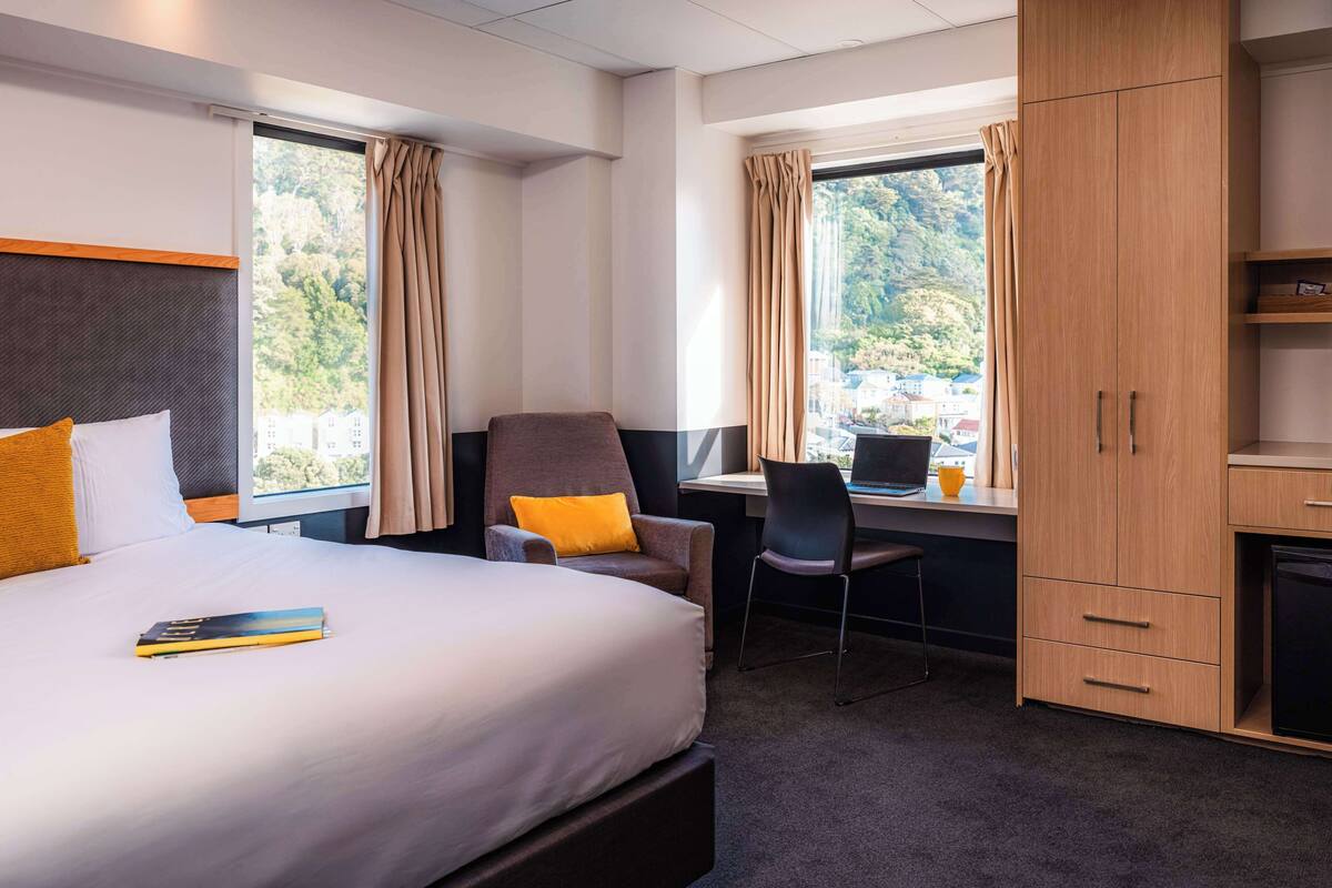 A hotel room with a bed, a desk, a chair, and a wardrobe.