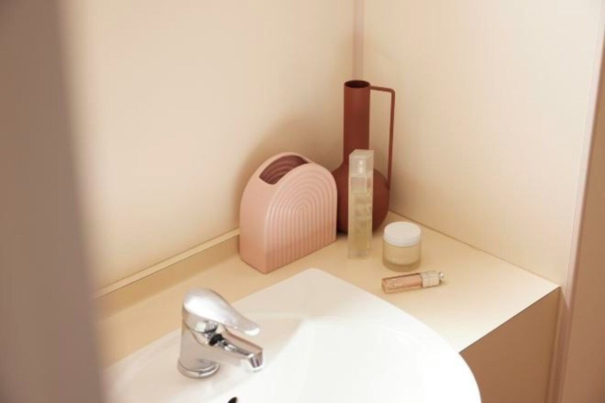 A bathroom with a white sink, a silver faucet, a pink soap dispenser, a cylindrical container, and a small bottle.