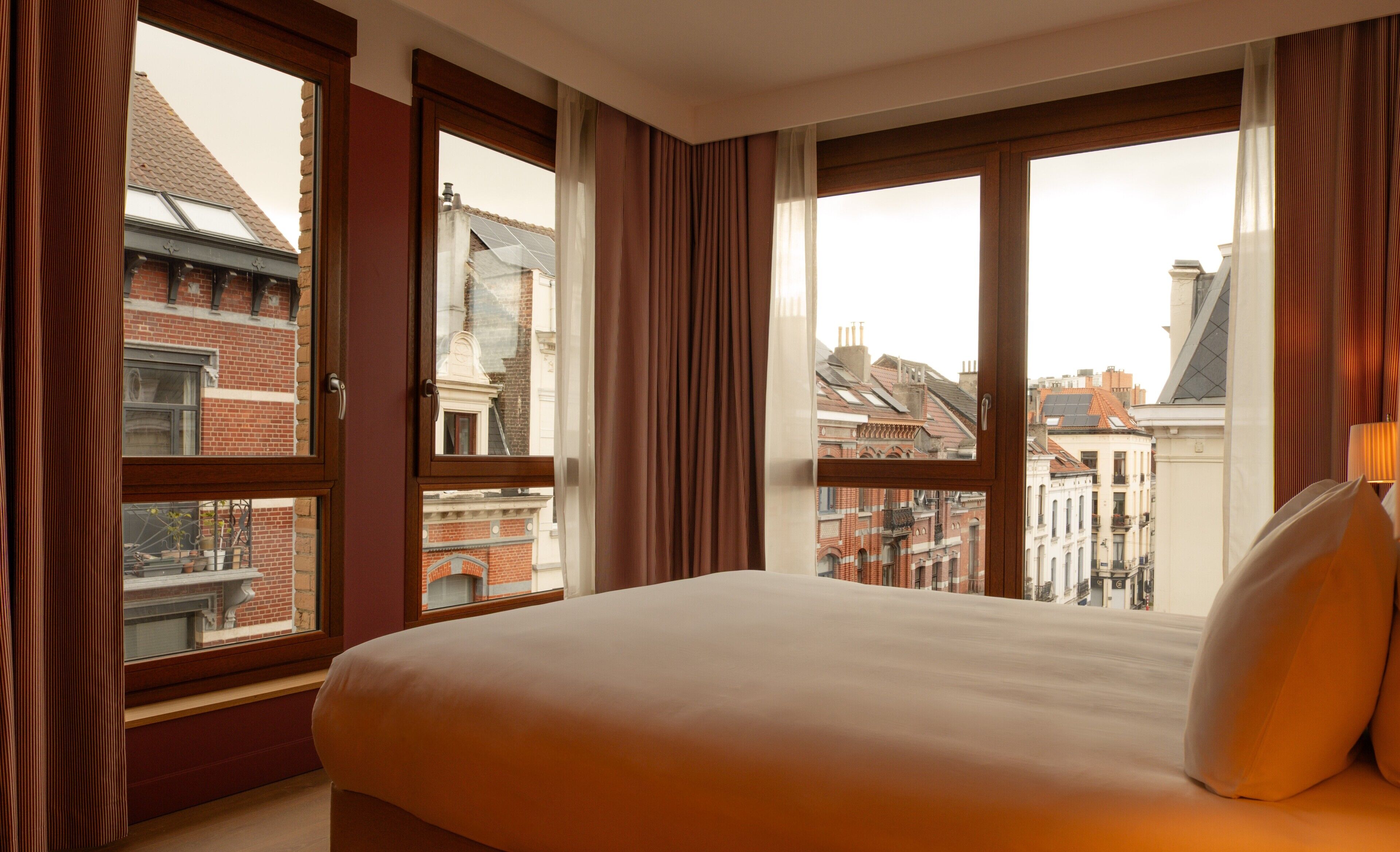 A hotel room with a large bed, multiple windows, and a view of city buildings.
