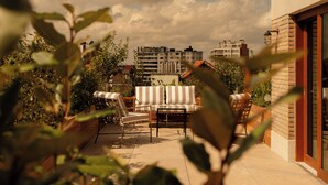 A rooftop terrace with a sofa and chairs, surrounded by plants, overlooking a cityscape. - 9Hotel Chelton (Brussels)