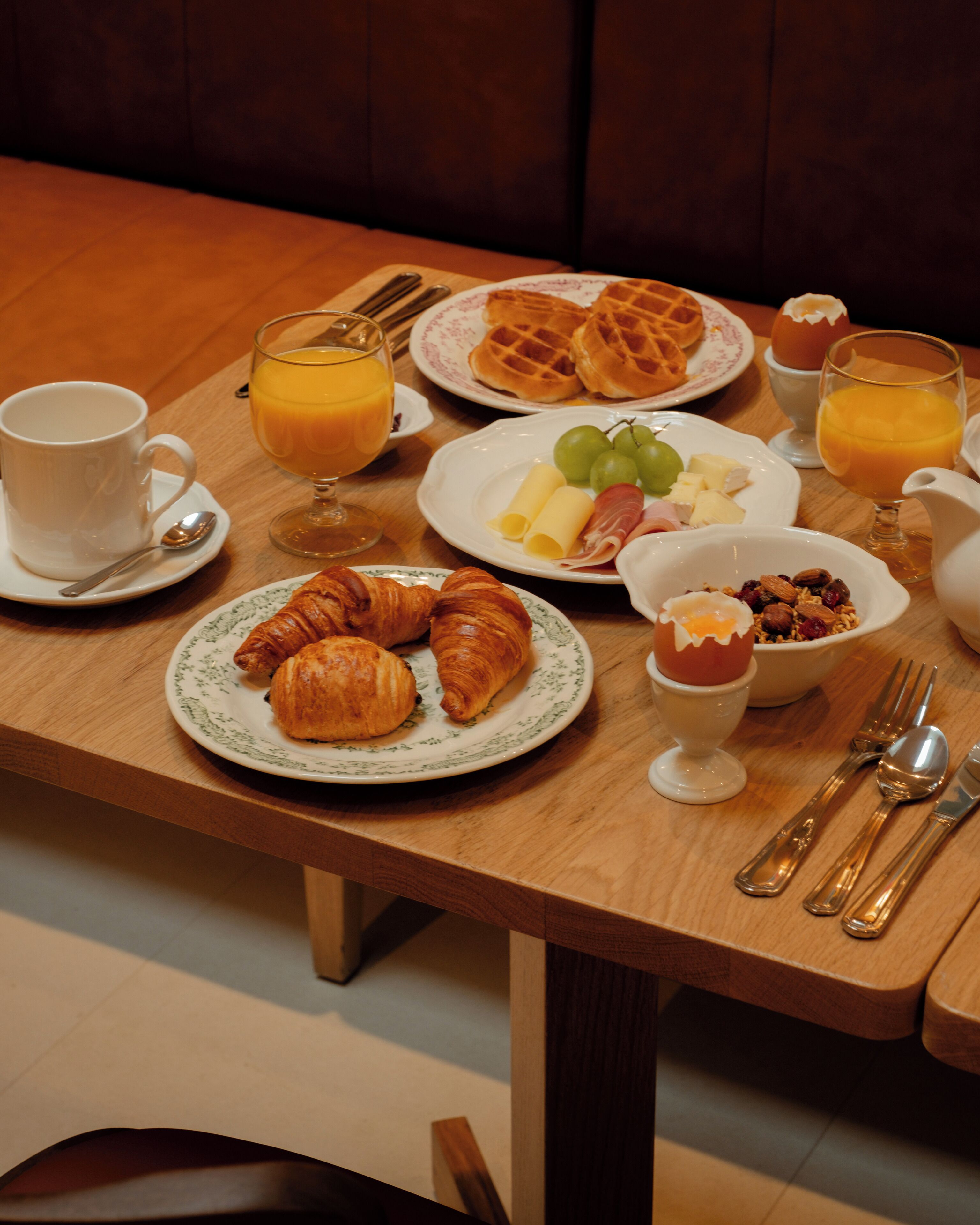 A breakfast table with croissants, waffles, fruit, and orange juice.