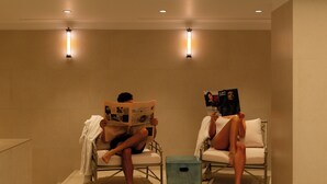 Two individuals seated in a spa-like setting with a glass floor, reading magazines. - 9Hotel Chelton (Brussels)