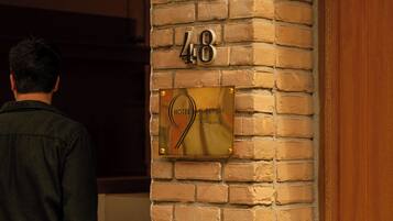 A hotel entrance with a brick wall, a number plaque, and a sign indicating the hotel name.