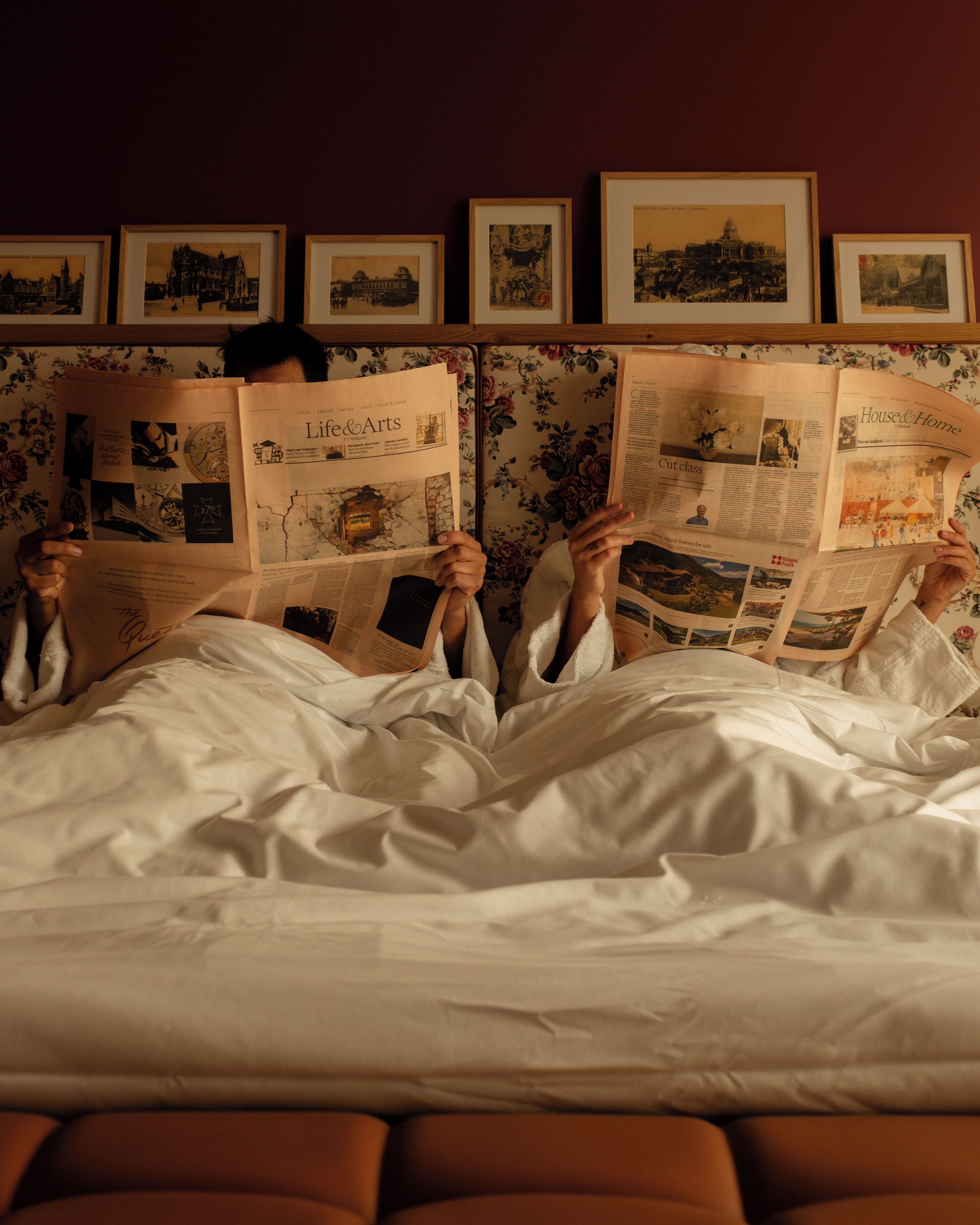 Una persona recostada en la cama leyendo un periódico.