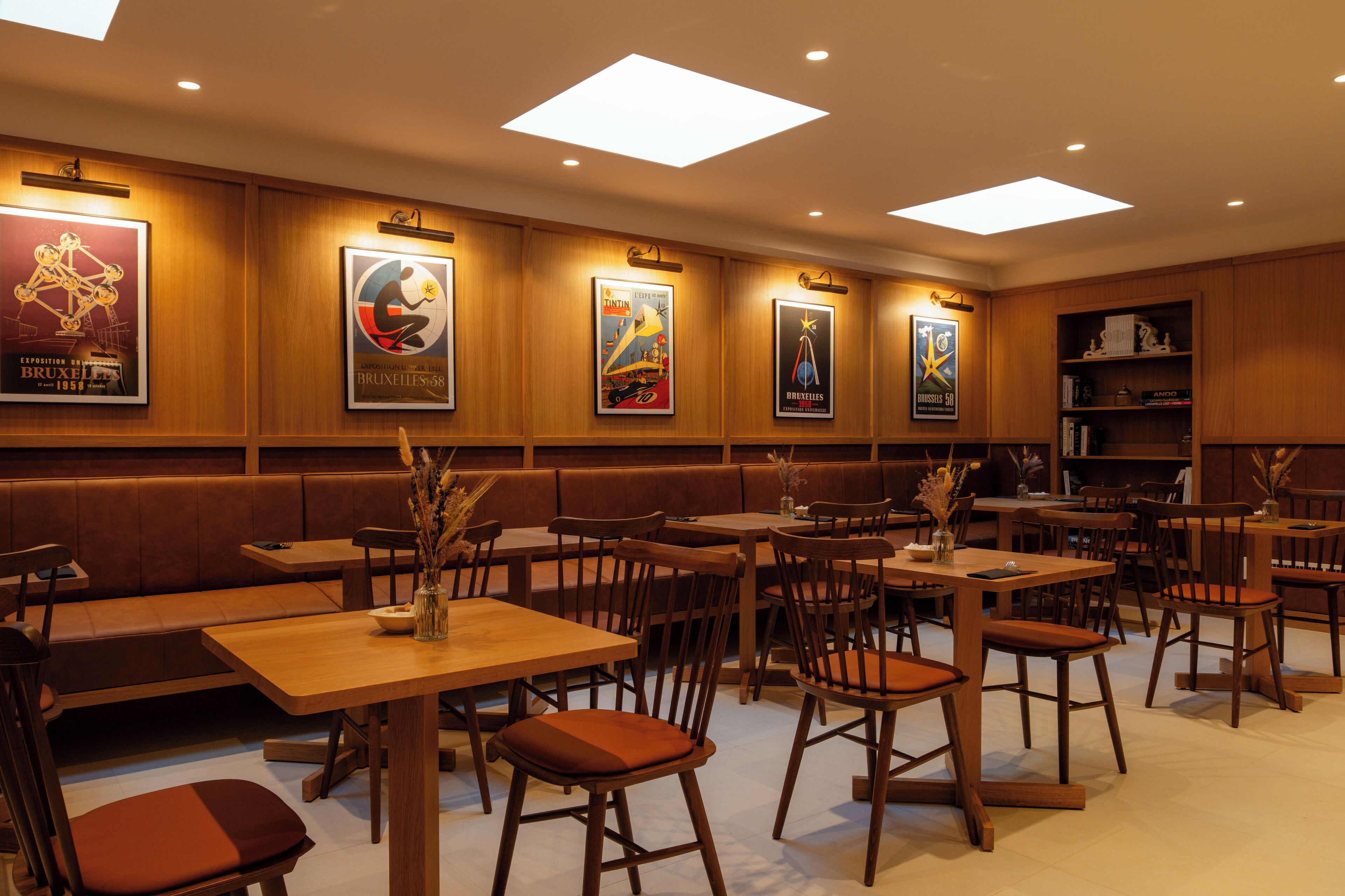 A restaurant with wooden booths, tables, and chairs. There are posters on the walls and a bookshelf in the corner.