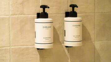 Two CODAGE Paris shower gel bottles mounted on a tiled wall.