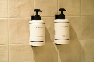 Two CODAGE Paris shower gel bottles mounted on a tiled wall.