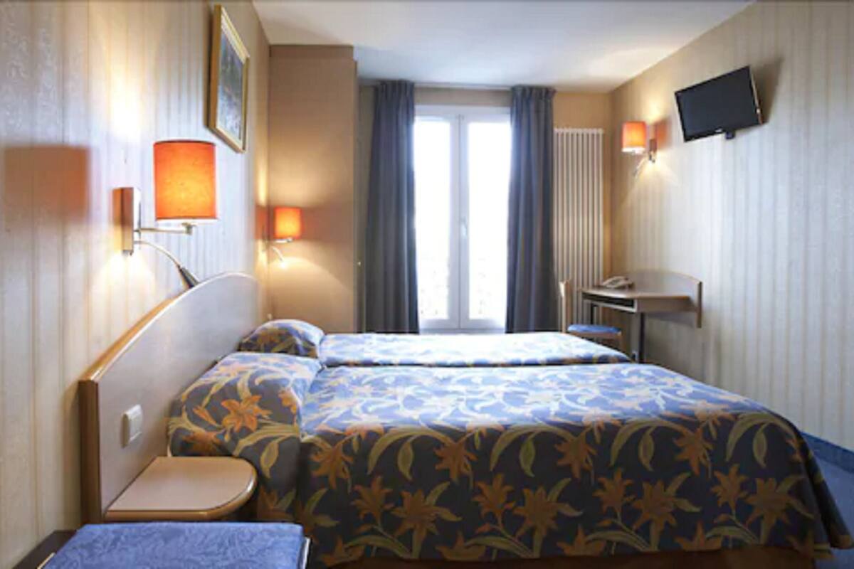 Ein Hotelzimmer mit zwei Betten, einem Schreibtisch, einem Sessel und einem an der Wand befestigten Fernseher.