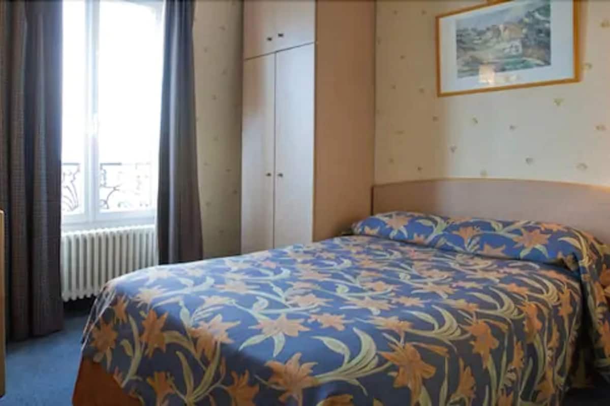 Ein Hotelzimmer mit Bett, Heizkörper, einem fensterbelaubten Fenster und einem gerahmten Bild an der Wand.