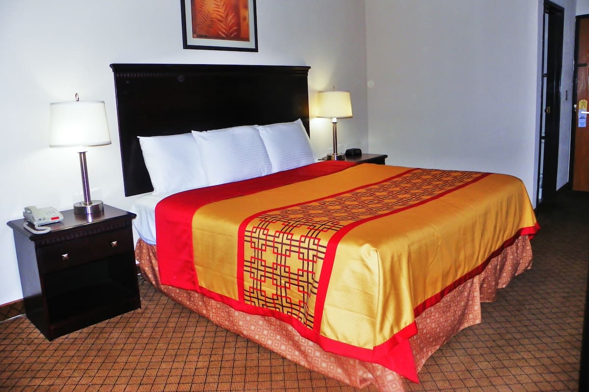 A hotel room with a large bed, two bedside tables, a nightstand, a lamp, and a framed picture on the wall.