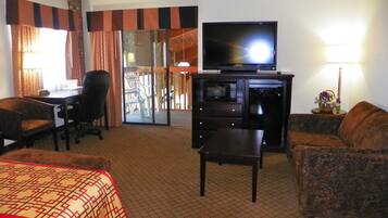 A hotel room with a bed, a desk, a television, a sofa, and a dining area with chairs and a table.