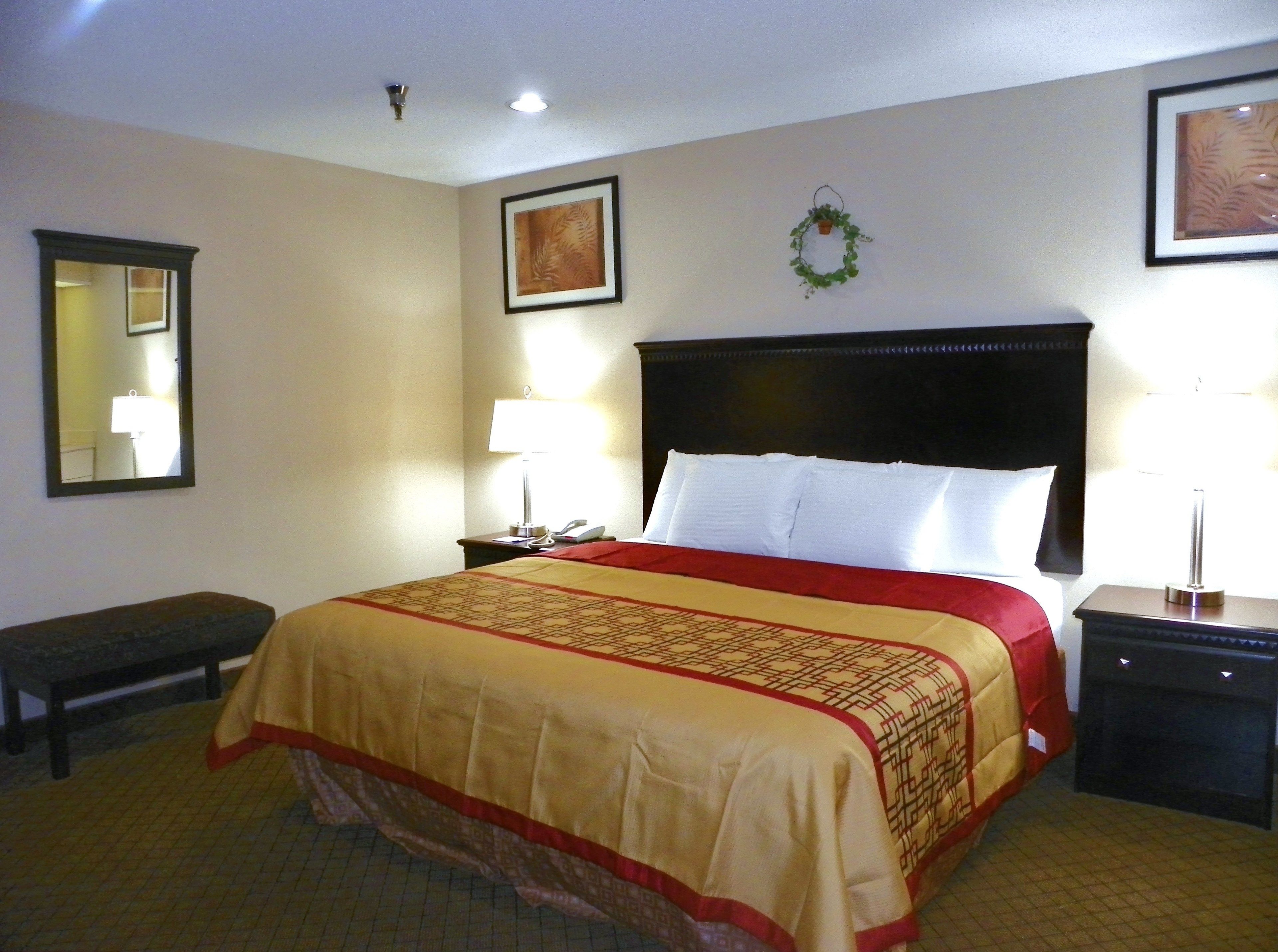 A hotel room with a large bed, two bedside tables, a nightstand, a mirror, and a framed picture on the wall.