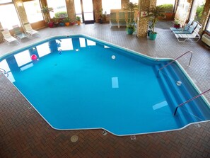 An indoor swimming pool with a blue water surface, surrounded by lounge chairs and potted plants.