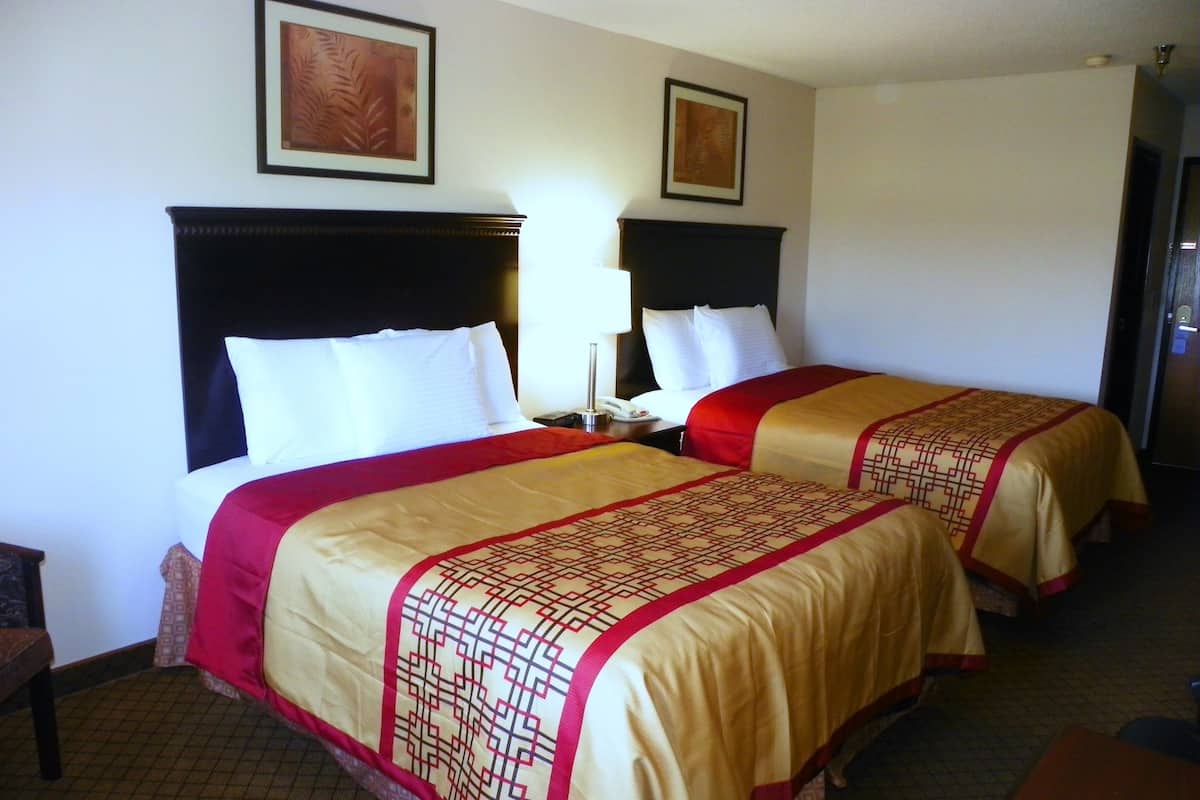 A hotel room with two beds, each with a headboard, a bedside table with a lamp, and a framed picture on the wall.