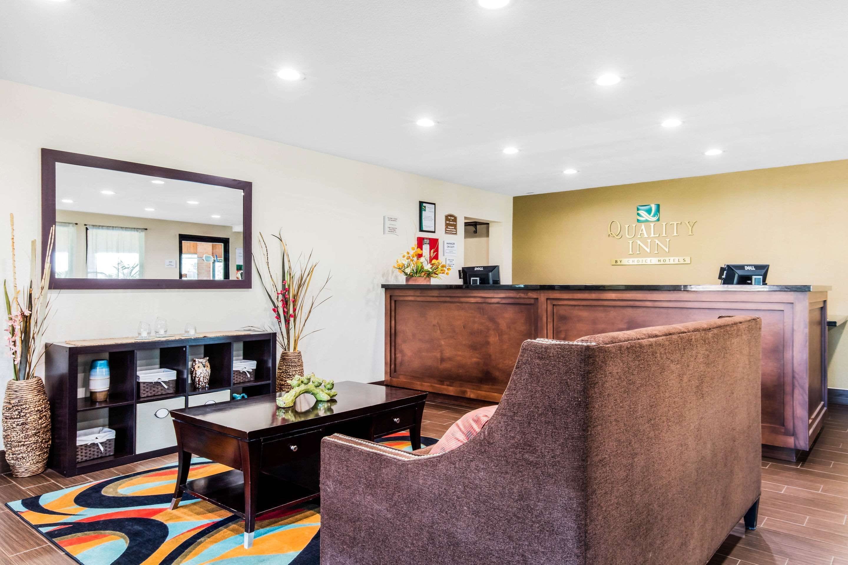 A hotel reception area with a reception desk, a large mirror, a sofa, and a decorative vase.