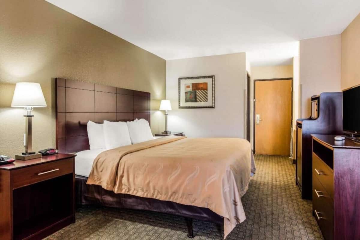 A hotel room with a bed, bedside lamps, a television, a dresser, and a framed picture on the wall.