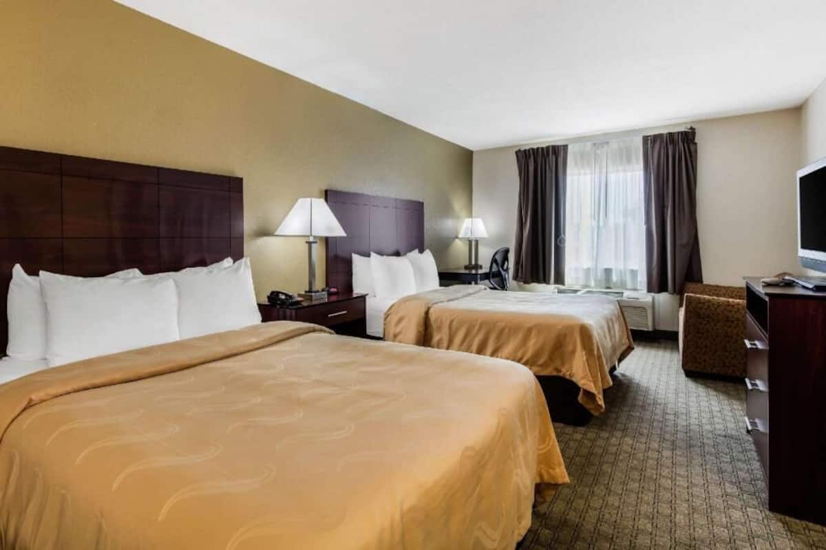 A hotel room with two beds, a desk, a chair, a television, and a window with curtains.