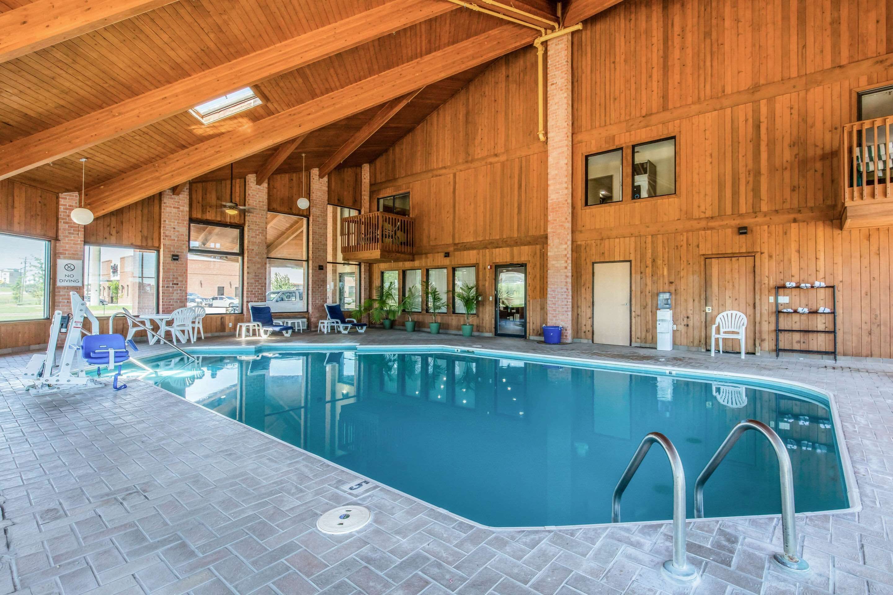 Une piscine intérieure avec un plafond en bois et des murs en briques, entourée de chaises longues et de plantes en pot.