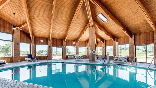Una piscina interior con vigas de madera y paredes de ladrillo, rodeada de sillones y mesas.