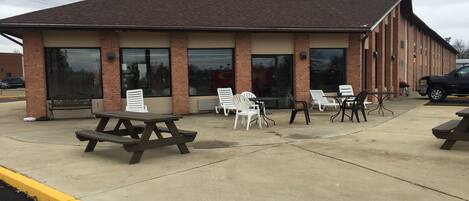 A building with a brick facade, large windows, and outdoor seating with picnic tables and chairs.
