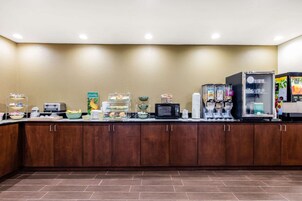 Zona de desayuno de hotel con microondas, máquina de café y mostrador refrigerado.