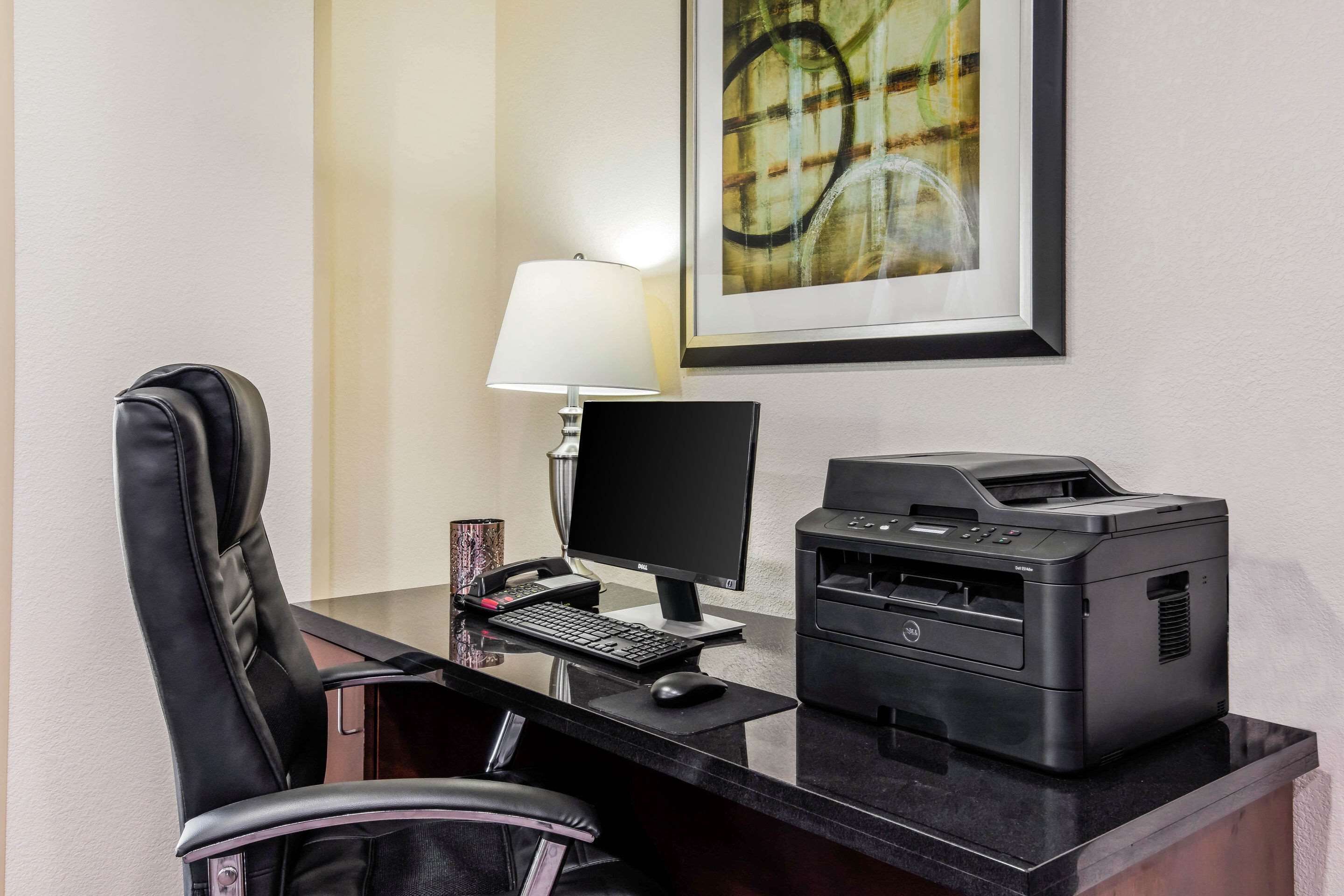 Un bureau d’hôtel équipé d’un bureau, d’un ordinateur, d’une imprimante et d’un tableau abstrait encadré accroché au mur.