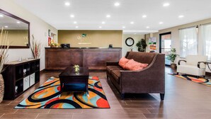 Un vestíbulo de hotel con una recepción, un sofá marrón con un cojín rojo, una mesa de centro negra y una alfombra colorida.