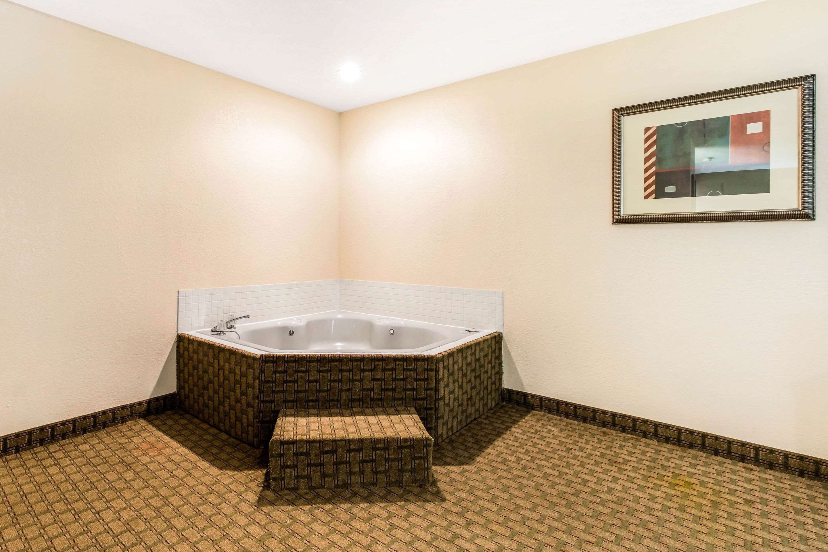 A corner bathroom with a freestanding bathtub, a small bench, and a framed abstract painting on the wall.
