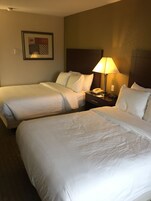 Habitación de hotel con dos camas individuales, una mesita de noche con lámpara, un teléfono y un cuadro en la pared.