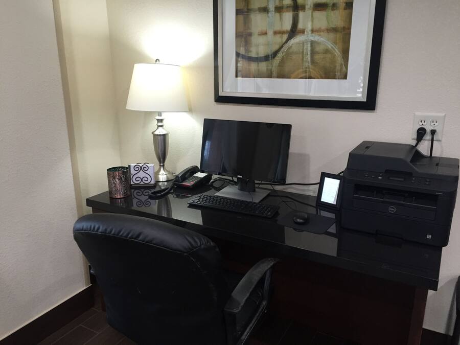 A hotel desk with a computer, printer, lamp, and a framed picture on the wall.