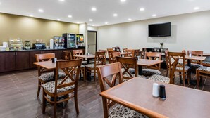 Un comedor de hotel con varias mesas y sillas, una máquina de café y un televisor montado en la pared.