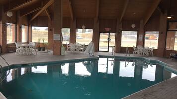 Una piscina interior con agua cristalina, rodeada de sillas y mesas de plástico blanco.