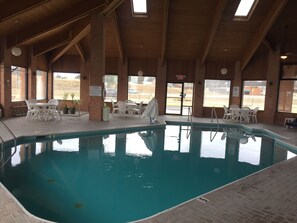 An indoor swimming pool with clear water, surrounded by white plastic chairs and tables.