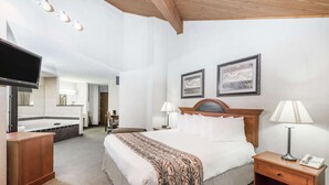 Une chambre d’hôtel avec un grand lit, des lampes de chevet, une table de chevet en bois, un téléviseur et deux tableaux encadrés au mur.