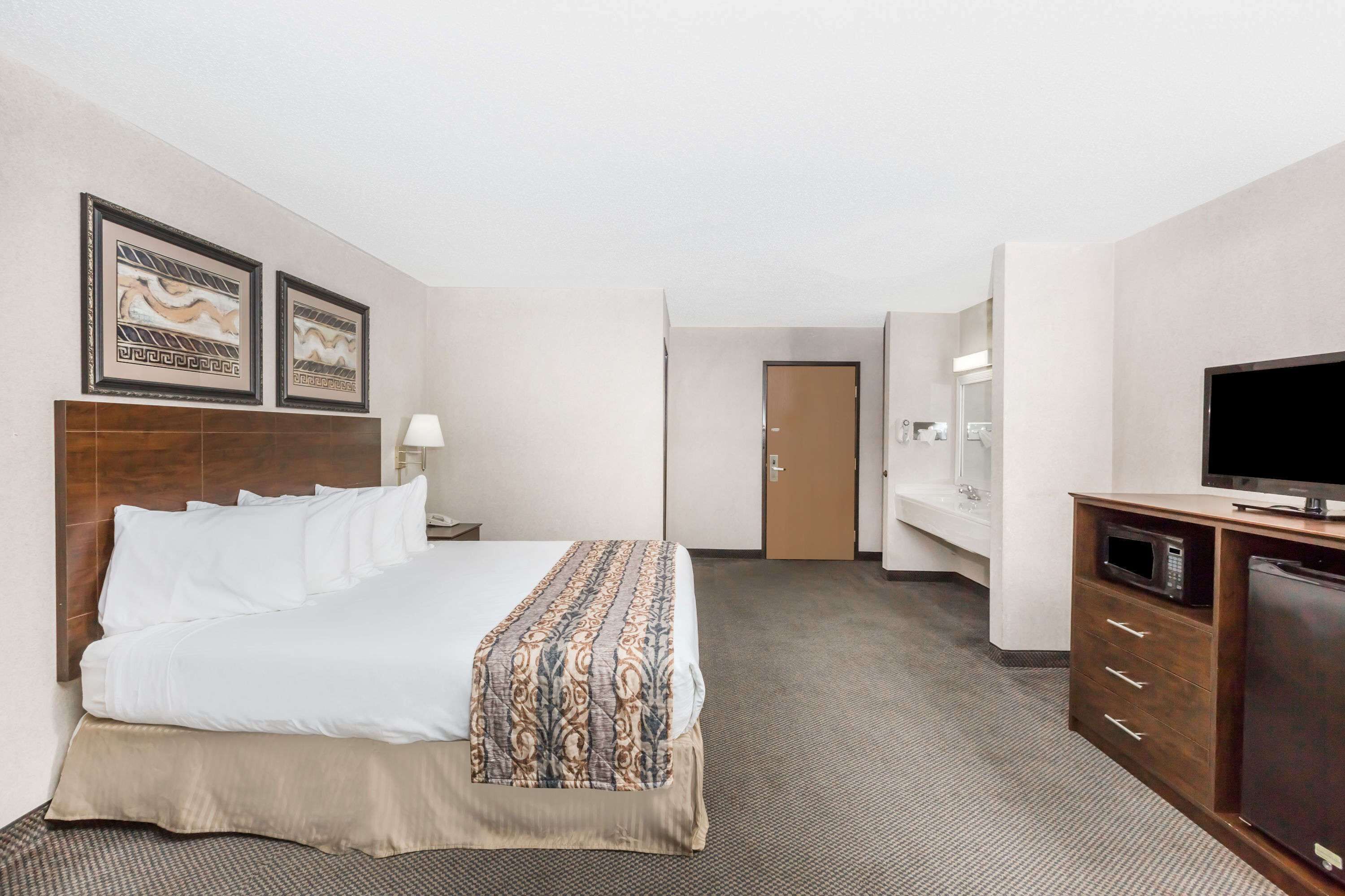 A hotel room with a bed, a TV, a microwave, and a door leading to another room.
