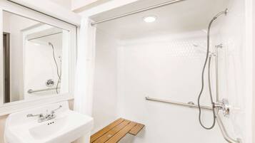 Un baño con un lavabo blanco, un espejo, una ducha con cabezal de ducha manual y un estante de madera.