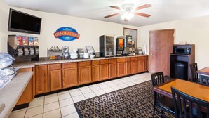 Un comptoir de petit-déjeuner avec une enseigne indiquant « Baymont Breakfast Corner », un ventilateur de plafond et un four à micro-ondes placé au-dessus d’un meuble.
