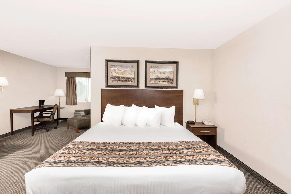 Une chambre d’hôtel avec un grand lit, un bureau, une chaise et deux tableaux encadrés au mur.