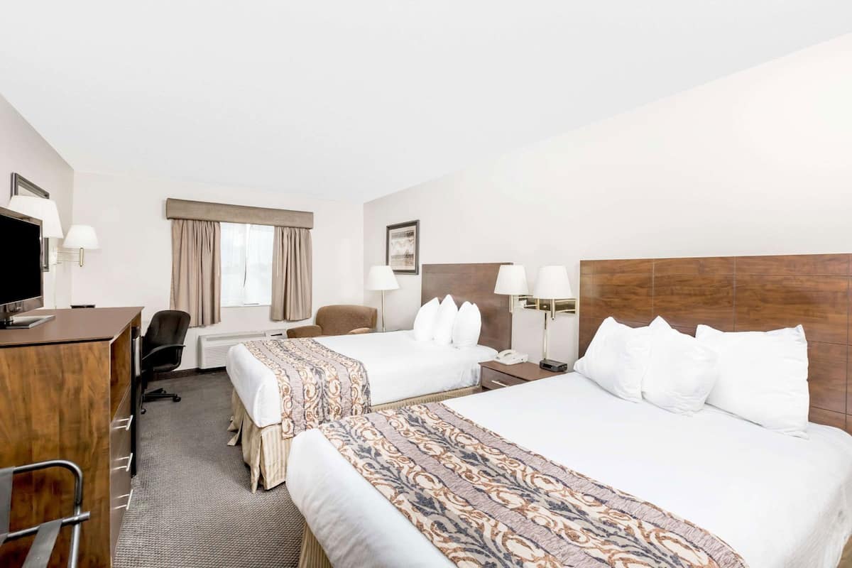 Une chambre d’hôtel avec deux lits, un bureau, une chaise, une télévision et une fenêtre avec des rideaux.