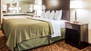 Habitación de hotel con una cama grande, una mesita de noche con lámpara, un espejo y vistas del vestíbulo del hotel.