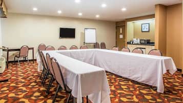 A conference room with a long table, chairs, a whiteboard, a TV, and a coffee station.