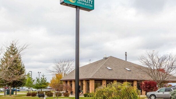 A Quality Inn & Suites sign, a brick building with a sloped roof, and a parking lot with cars.