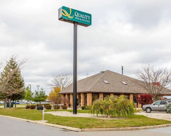 A Quality Inn & Suites sign, a brick building with a sloped roof, and a parking lot with cars.