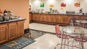 Un vestíbulo de hotel con una recepción, zona de buffet y área de descanso con mesas y sillas de vidrio.